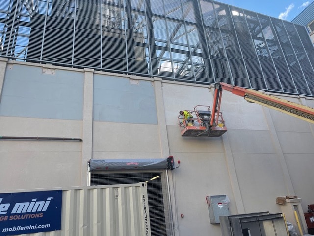 Worker on boom lift applying stucco to large commercial exterior